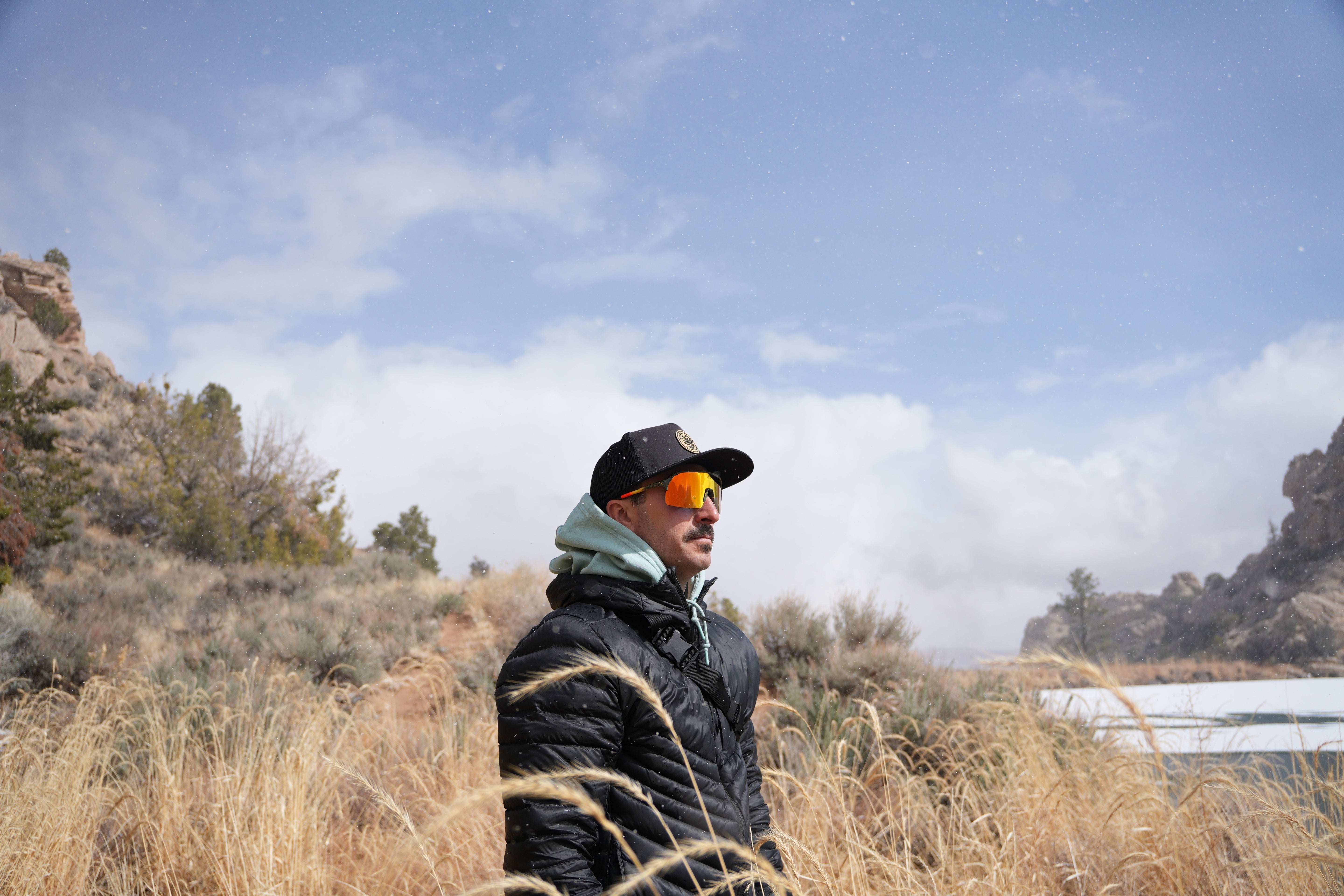A man wearing Fats Brook Trout Sunglasses near a small pond.